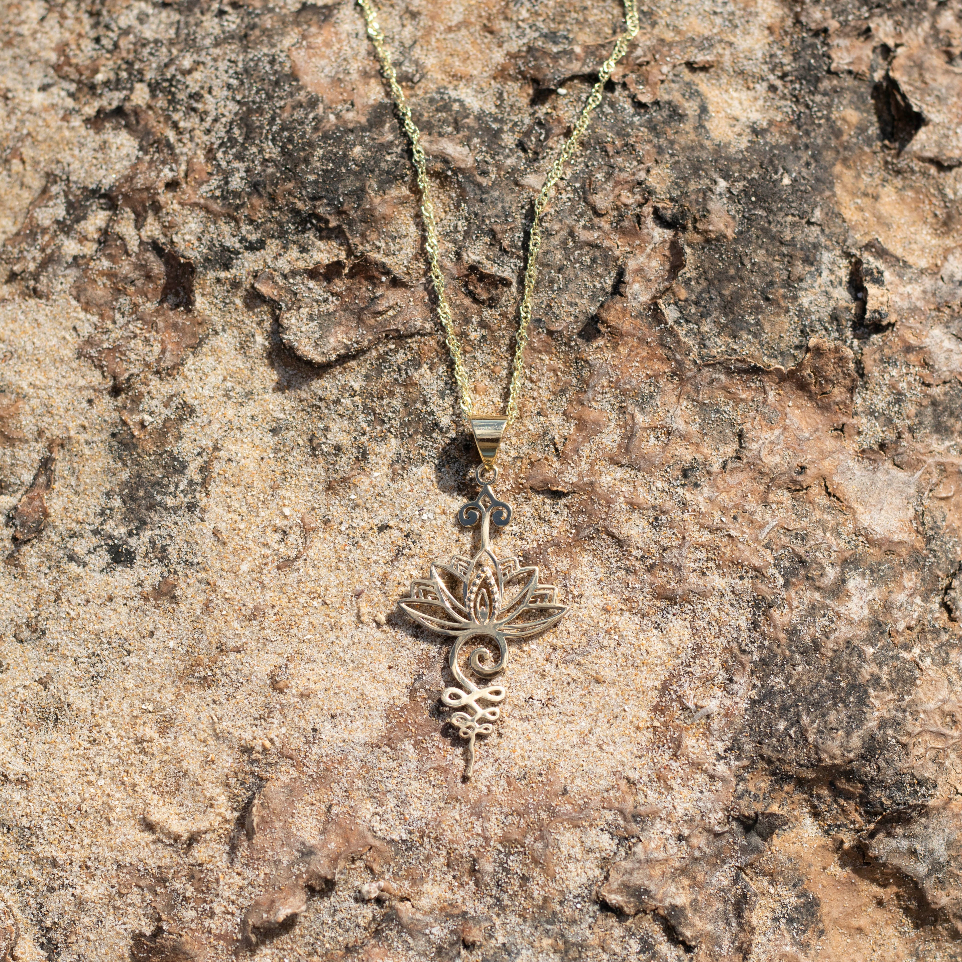 Colgante loto unalome dorado sobre rocas